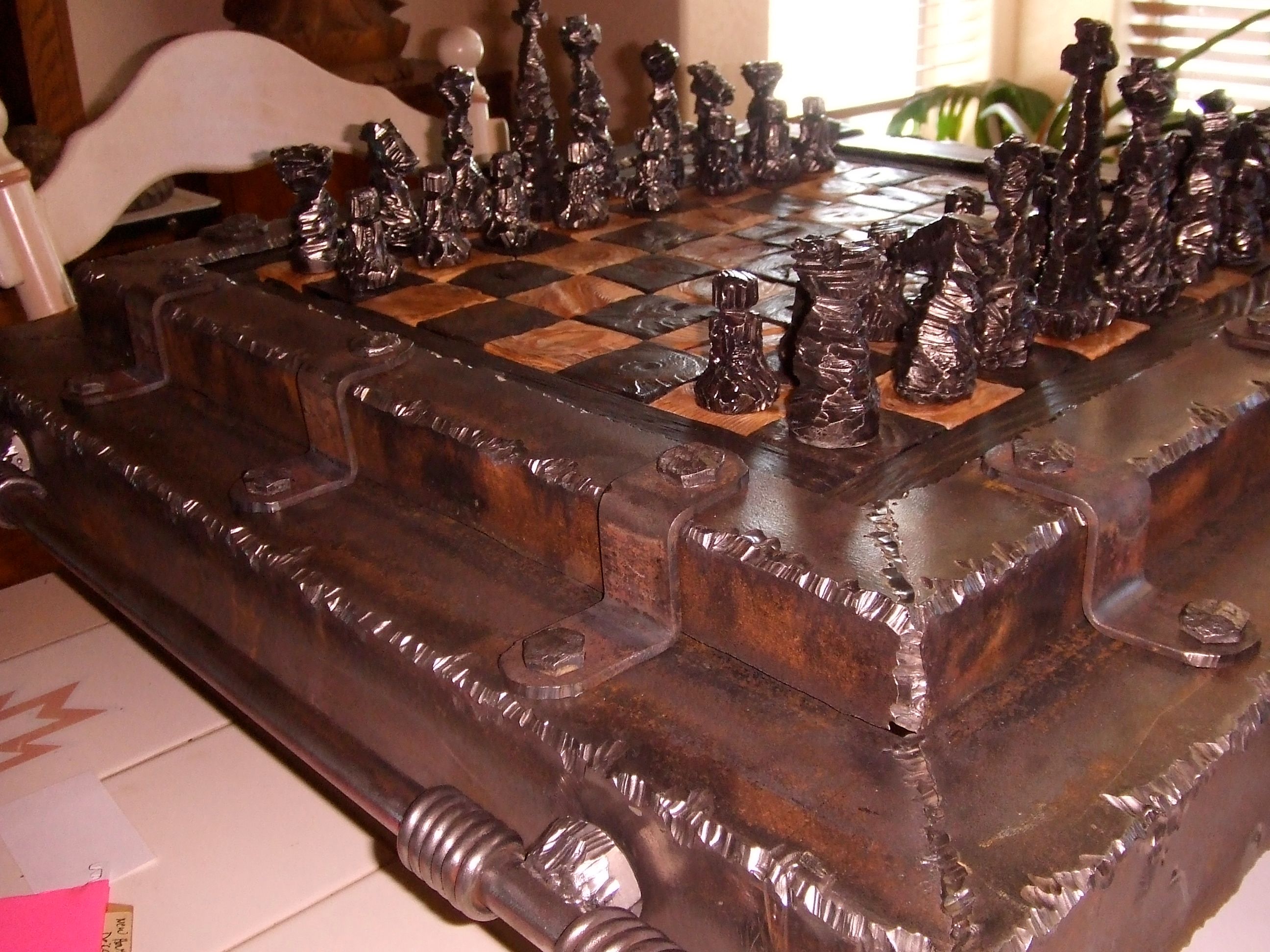 A low view of a chess board in a heavy dark frame with rolled steel trim, the pieces lined up on light and dark squares.