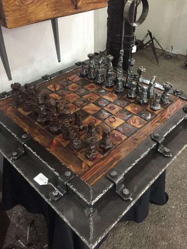 A chess set on a board framed in steel with weld beads and strap brackets, seen from one corner.