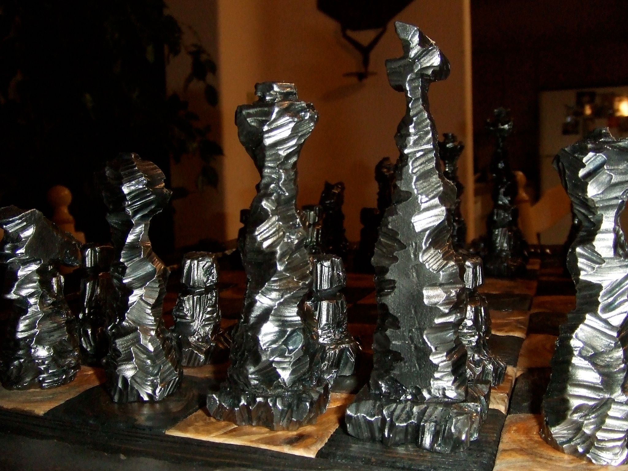 Silver chess pieces with rough, crumpled surfaces, a tall king among them, on wood-grain squares.