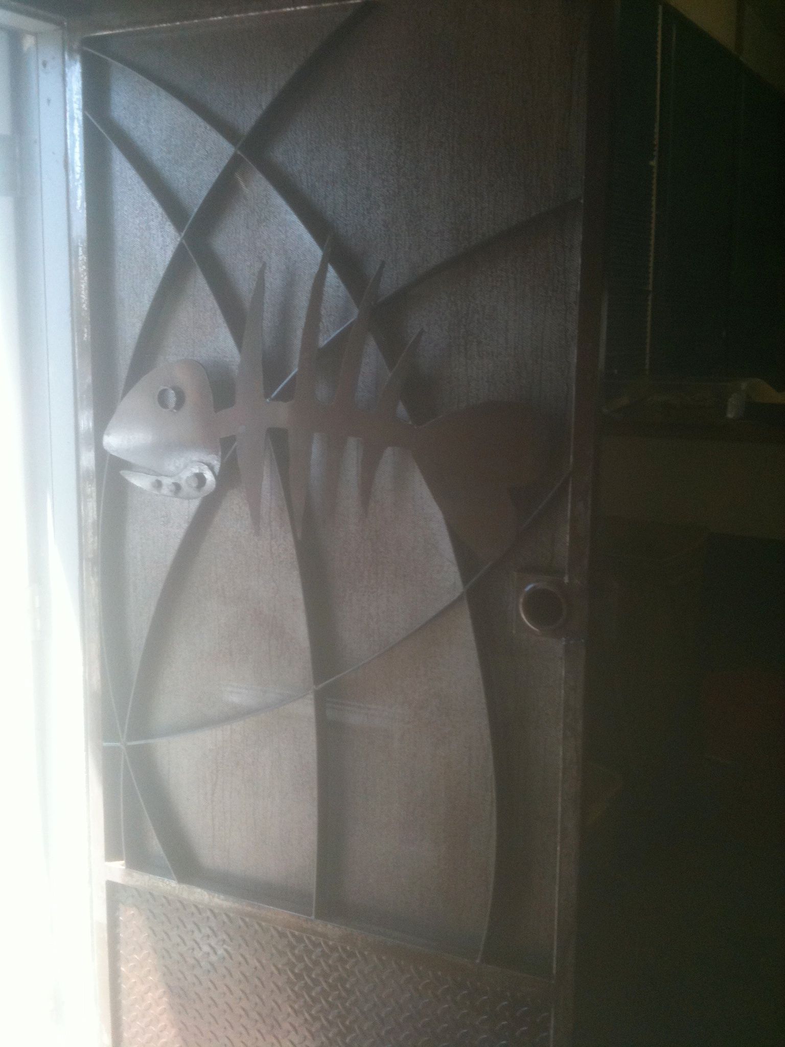A black steel door with large curling scrolls lying on a stand outdoors, with a truck and trees behind.