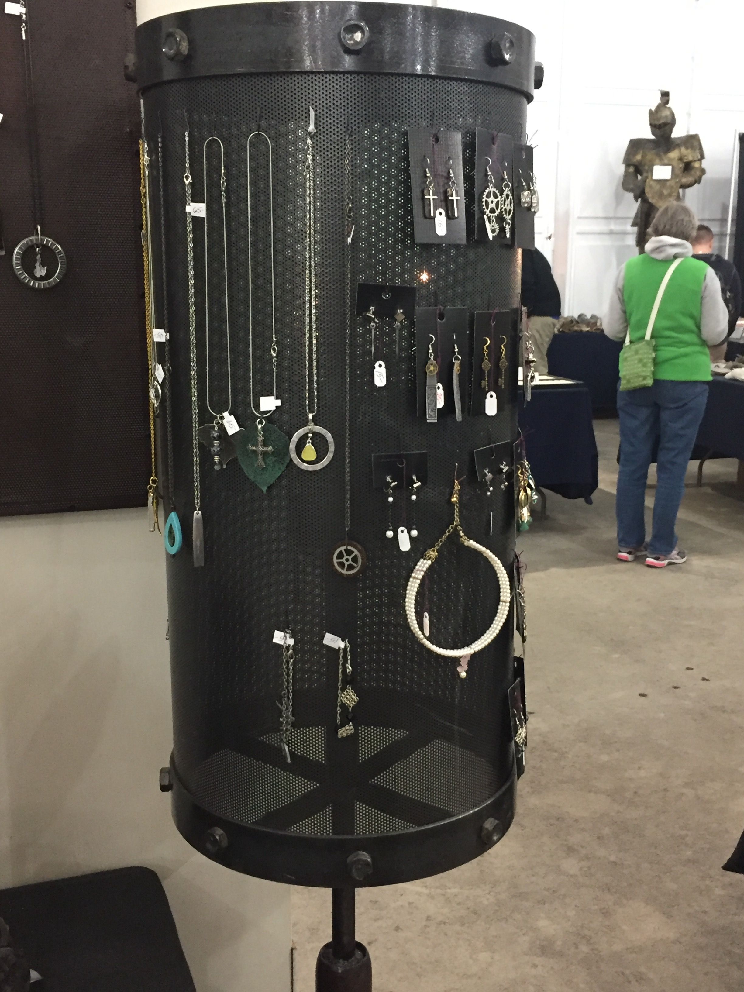 A row of long necklaces with pendants hung on a black panel, beside the edge of a cylinder stand.