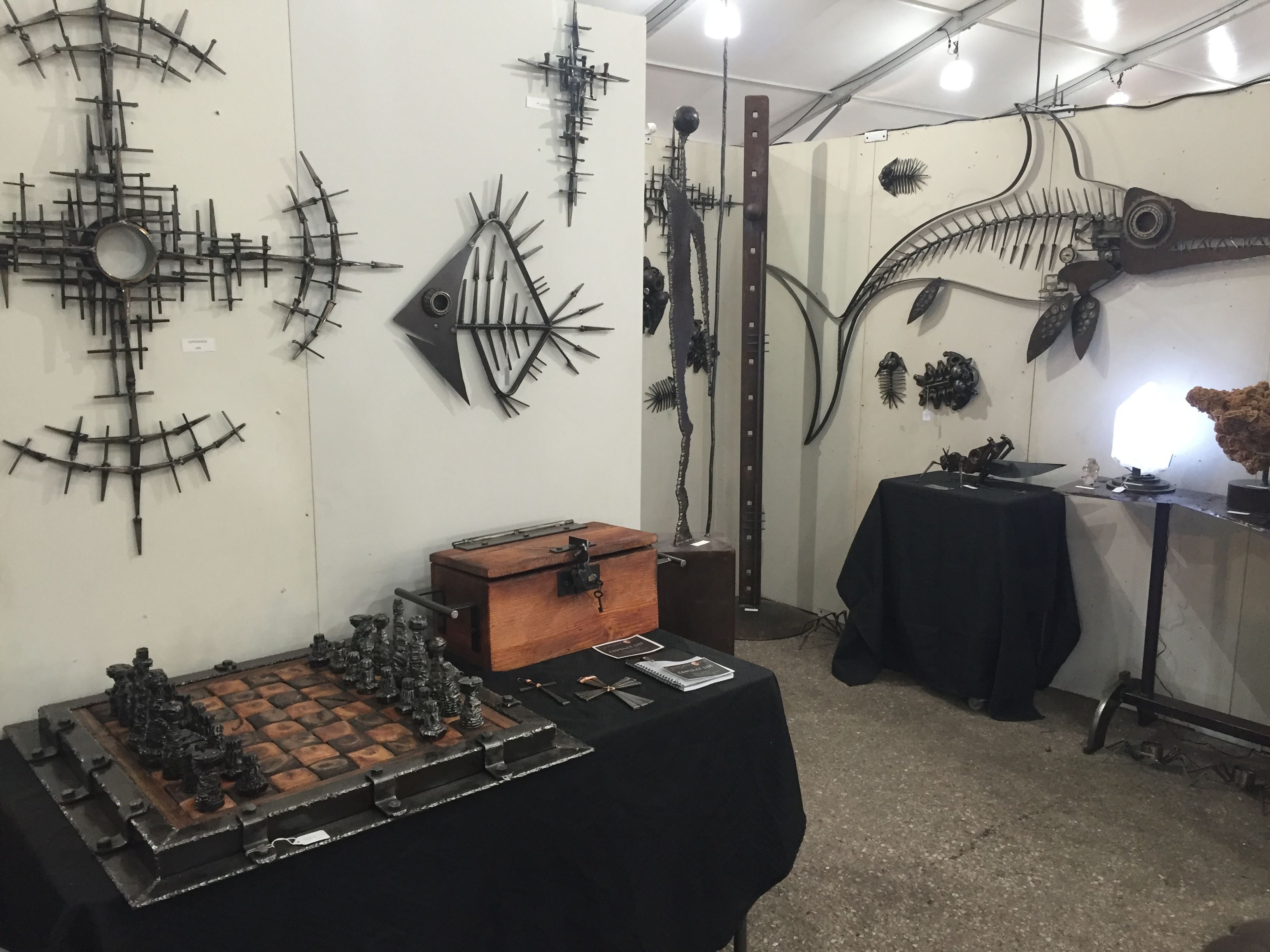 White booth walls hung with a steel sunburst, a fish skeleton and a long swordfish shape, above a black table holding a chess set and a wooden box.