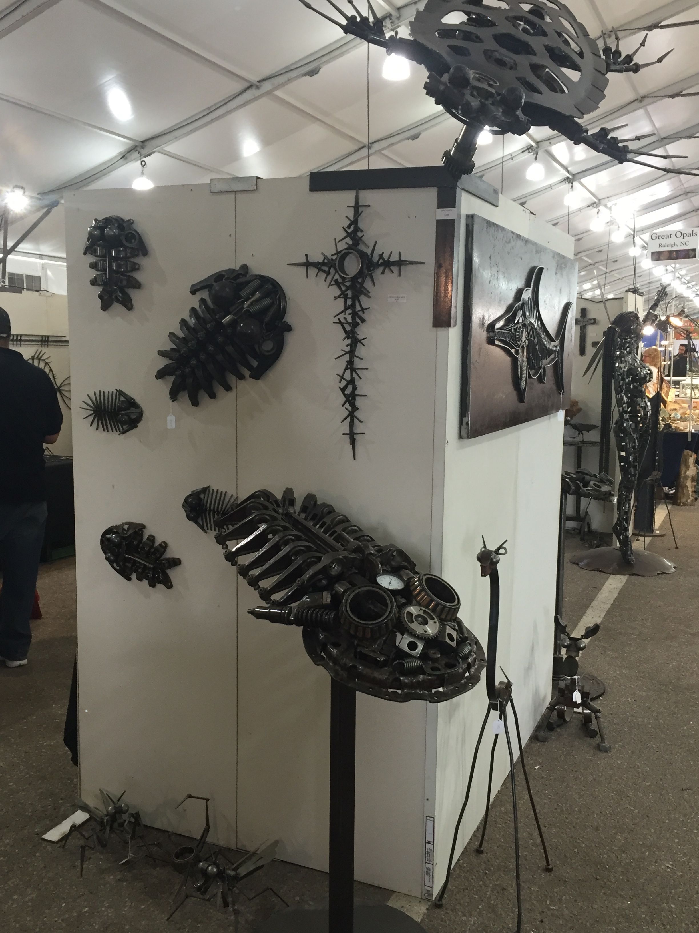 The corner of a white booth wall with trilobite and fish pieces, a cross, and a large many-legged steel creature set on top.