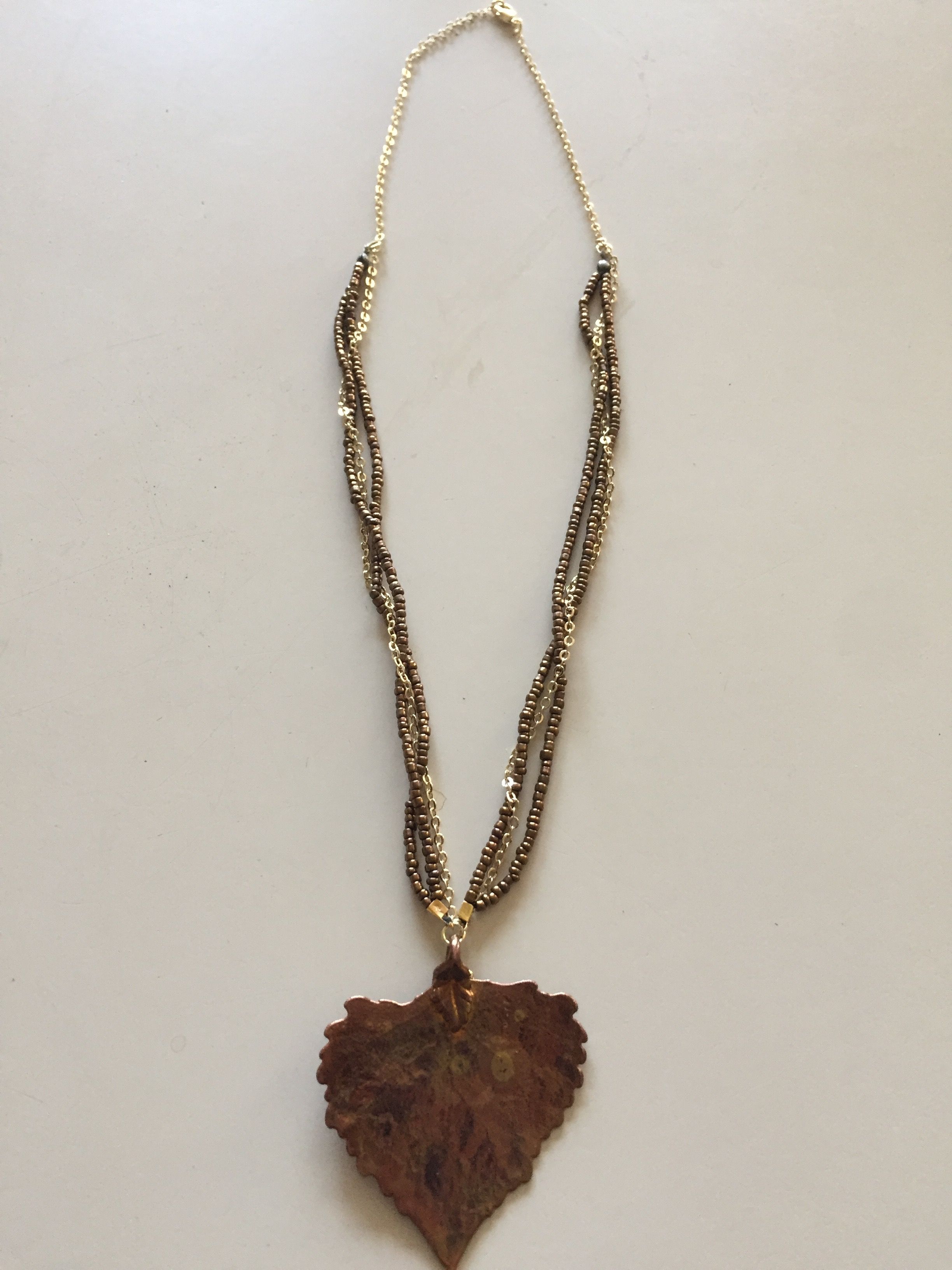 A copper leaf pendant on a twisted beaded chain, laid out on a white background.