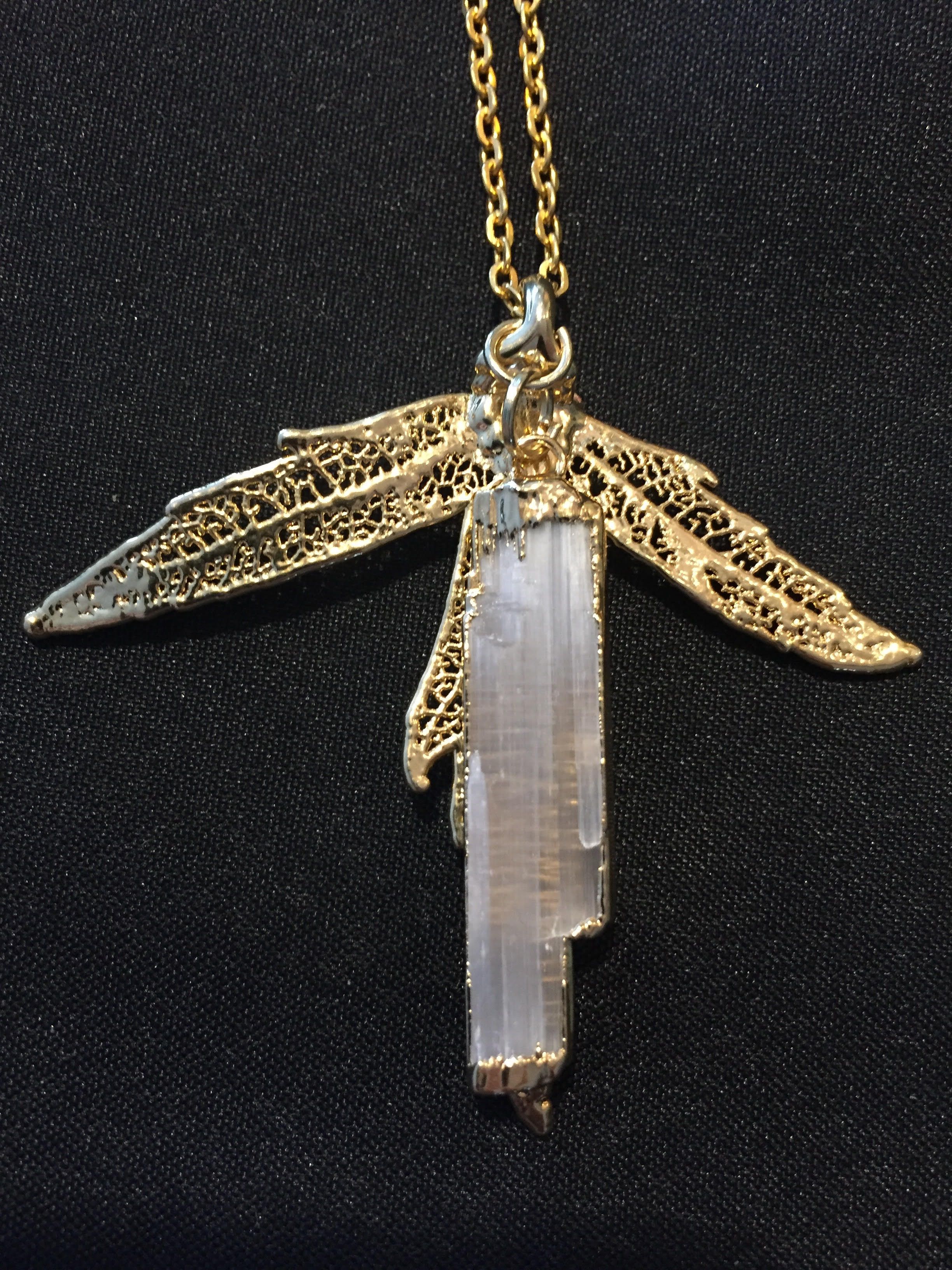 Two gold leaf skeletons spread like wings behind a long white crystal, on a gold chain.