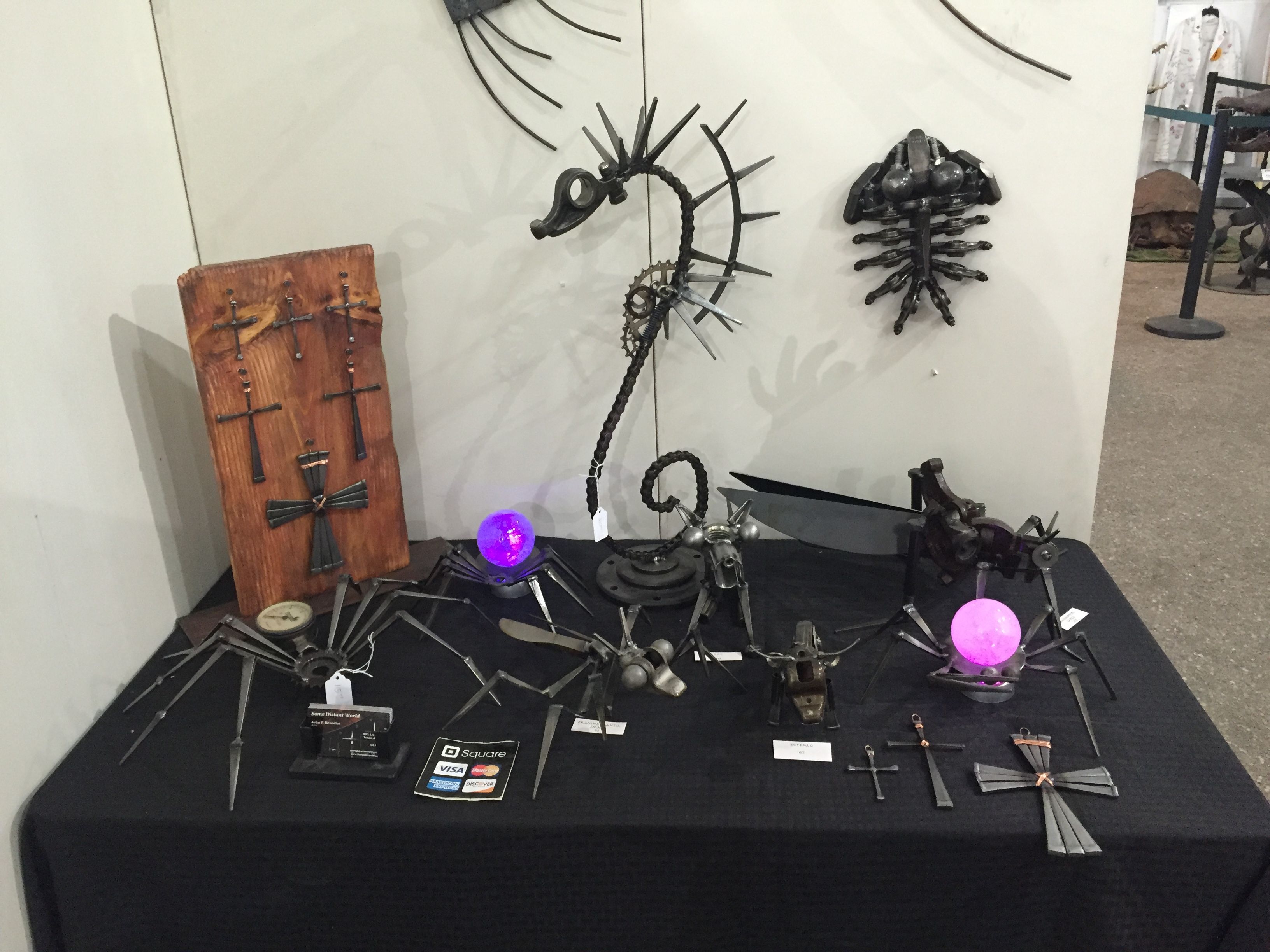 A black table with small metal pieces, two glowing purple globes and a seahorse, with crosses mounted on a wooden plaque to the left.